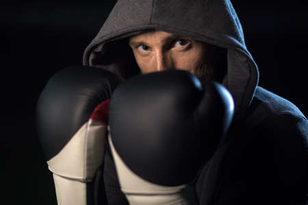 Strong man in a gray hooded in black and white boxing gloves on his hands covers the face. Horizontal photoの写真素材