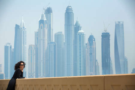 Elegant dark-haired girl in black dress on the background of skyscrapers in Dubai. Admiring the views. UAE. Horizontal photoの写真素材