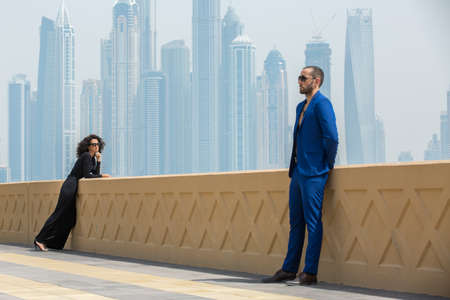 Young couple on the terrace with views of the skyscrapers in Dubai. The man in the blue suit. The dark-haired girl in a long black dress. UAEの写真素材