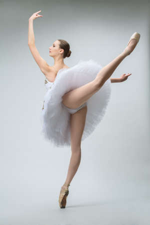 Young ballerina in white tutu shot in the studio on a white background. Dancer doing dance exercises. Choreographic pose is an attitude.の写真素材