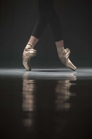 Legs of ballerina who stands on the pointes. Light falls down on her feet. Photo shoot in a low key.の写真素材