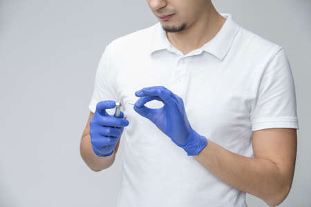 Male doctor in blue latex gloves and white t-shirt holding a dental handpiece and a dental bur in...