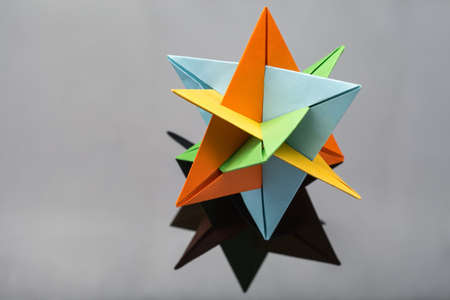 Kusudama star origami on a gray reflective background. Close-up photo. It colored in orange, yellow, blue and green. Horizontal.の写真素材