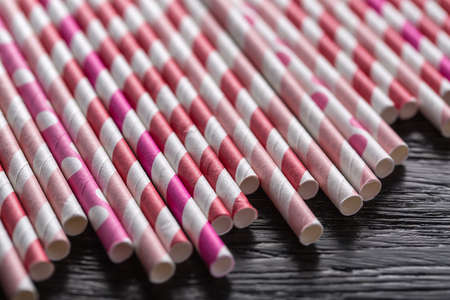 Many colorful straws lying on a dark textured surface. Straws are red and white, pink and white, purple and white. There is free space below the straws. Close-up photo. Horizontal.の写真素材