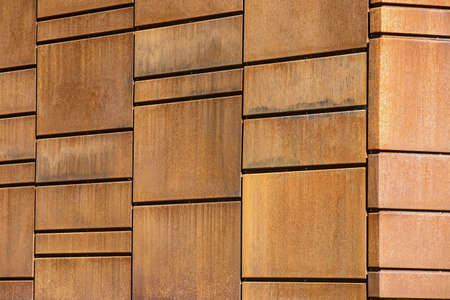 Wall is lined with the orange rusty metal tiles. Photographed at an angle outdoors. Horizontal.