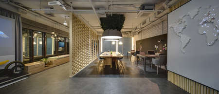 Interior in a loft style. There are tables and chairs. There are notebooks, laptops, holders with...