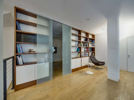 Hall with light walls and a light parquet on the floor. There are brown-white bookcases with books and models of old airplane and bike. Between the bookcases there are frosted glass sliding doors. Big white ornamental round lamps reflected in the doors. Bの写真素材