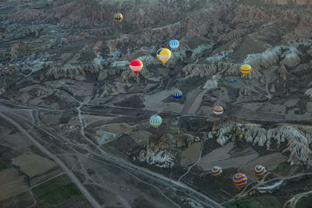 Multi-colored air balloons are flying above the roads and mountains in the valley. Balloons colored in red, white, blue, yellow, orange, green. On the left there is a part of a town. View from the top.の写真素材