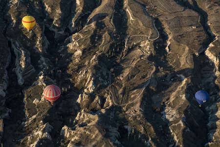 Multi-colored air balloons are flying above the mountains in the valley. Balloons colored in red, yellow, blue, white, gray. There is a road under them. View from the top.の写真素材