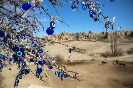 Naked tree with hanging decorations. Decorations are blue with image of the Fatima eye talisman. On the soft background there are horses, rock formation and the blue sky.の写真素材