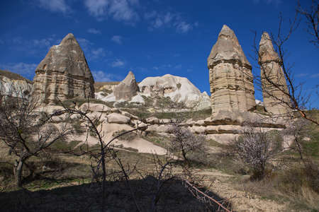 Rock formation with houses carved into rock on the blue sky with several clouds background. In the front there are several naked and blooming trees.の写真素材