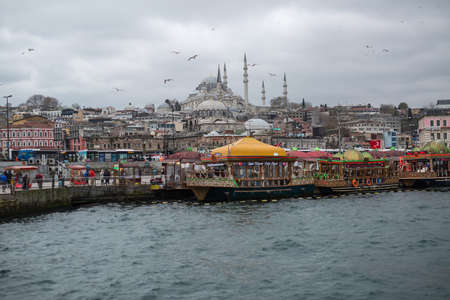 Several decorated ships in dock on the background of old town street, mosque and the gray cloudy sky. Many seagulls are flying in the air.のeditorial素材