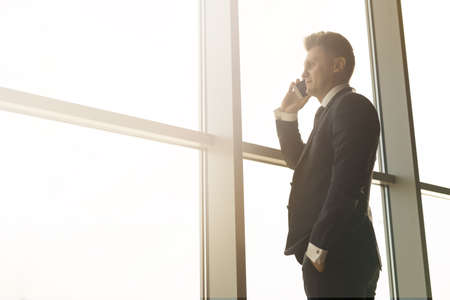 Stylish business man in the background of a large window in the floor. Model talking on the phone.の写真素材
