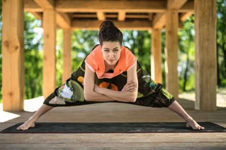 Amazing girl makes wide-legged forward bend on the black yoga mat on the wooden terrace on the...
