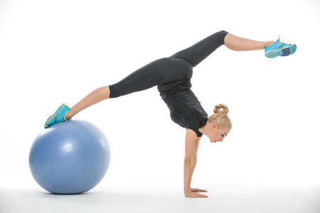 Sexy blonde girl in the sportswear with a blue fitball on the white background in the studio. She...