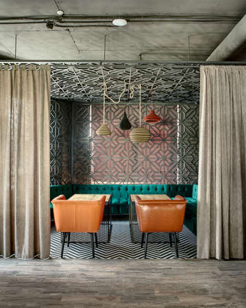Wonderful interior in a loft style in a mexican restaurant. There is a zone decorated with metal lattices and curtains. In the zone there are green sofas, brown chairs, wooden tables and multi-colored lamps over them. On the floor there is a gray parquet,の写真素材