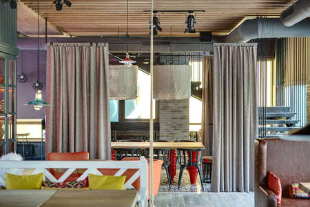 Mexican restaurant in a loft style. On the left there is a wooden table with white sofa with multi-colored pillows, a wooden table with orange chairs, a cupboard with glass doors. On the right there is a brown sofa with color pillows, a black stair. On thの写真素材