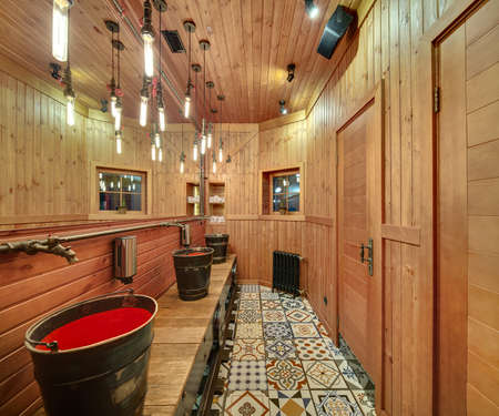 Washroom with wooden walls in a mexican restaurant. On the left there are metal-red washbasins in the form of buckets, soap dispensers, metal faucets in the form of a fairy animal, a big mirror. Opposite wall reflected in the mirror. On the back wall therの写真素材