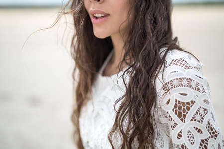 Portrait of a beautiful brunette in a white lace dress. Girl walking on sandy estuary looked like a desert.の写真素材