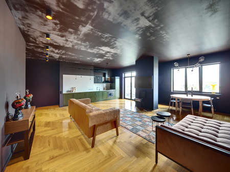 Interior in modern style with parquet and colorful carpet on the floor. There is green kitchen with equipment, sofas, table with candles, chairs, rack with lamps, column with TV, vinyl player, lamps.の写真素材