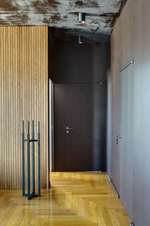 Room in a modern style with a parquet on the floor. On the left there is a wooden wall with black metal stand with black candles. On the right there are two doors. On the ceiling there are lamps.の写真素材