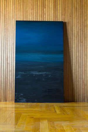 Blue picture leans on the wooden wall. There is a parquet on the floor. Indoors. Vertical.の写真素材