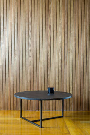 Dark wooden round table with metal legs on the background of the wooden wall. There is a dark glass box on the table. On the floor there is a parquet. Indoors. Horizontal.の写真素材
