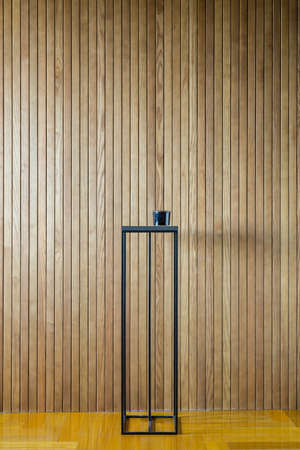 Black metal stand on the background of the wooden wall. There is a dark glass box on the stand. On the floor there is a parquet. Indoors. Vertical.の写真素材