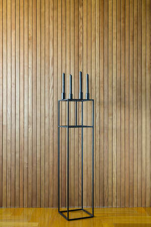 Dark metal stand with black candlestick with four black candles on the background of the wooden wall. On the floor there is a parquet. Indoors. Vertical.の写真素材