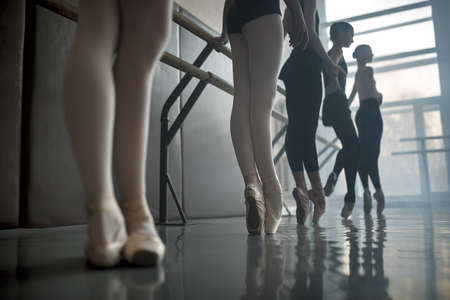 Young ballet dancers stands near the ballet barre at the ballet hall. Daylight falls on them through the large window.の写真素材