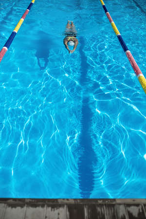 Active girl swims in the swimming pool. Swimmer wears a black-lime swimsuit, a white swim cap and...