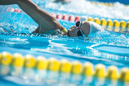Attractive close-up photo of female swimmer in the motion in the swimming pool outdoors. She wears a black-lime swimsuit, a white swim cap and swim glasses. Horizontal.の写真素材