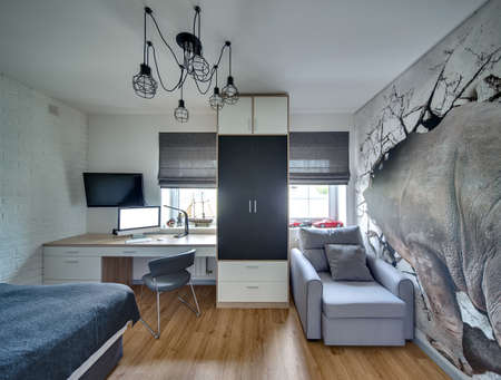 Bedroom in modern style with light walls and parquet on the floor. There are windows with roman curtains, table with computer, chair, TV, wardrobe, armchair and bed. At the top there is chandelier.の写真素材