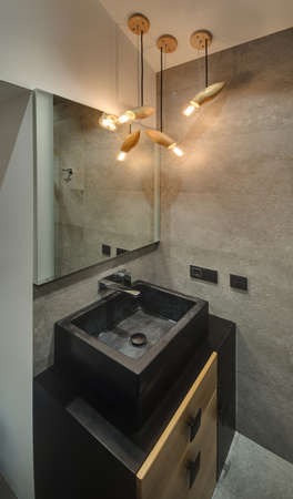 Fancy bathroom with gray textured tiles and glowing lamps. There is sink with tap and mirror. Under the sink there is locker. Vertical.の写真素材