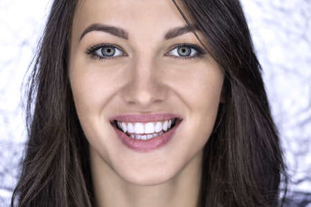 Beautiful girl with a broad smile looks into the camera on the blurry bright background. Close-up...