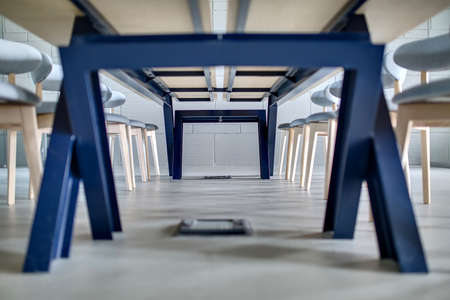 Light wooden table with blue legs and many wooden gray chairs around it on the background of the light brick wall. Daylight falls from the right. Indoor. Horizontal.の写真素材