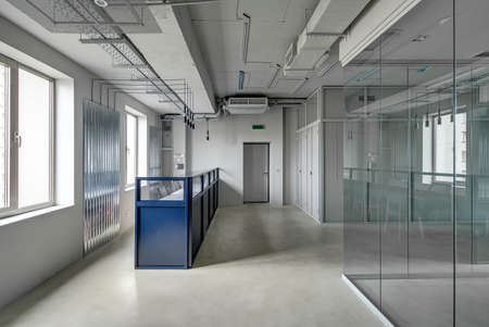 Blue metal reception rack with armchairs in a loft style office with gray walls. There is an...