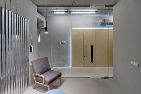 Business interior in a loft style with gray walls. There is a room with a glass partition with door,...