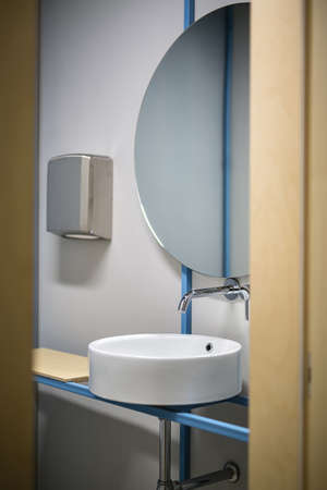 Entrance to the restroom in the office. There is a white sink with a faucet and a mirror over it, a tissue dispenser and a wooden tabletop. Closeup. Vertical.の写真素材