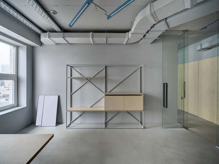 Business room in a loft style with gray walls. There is a window, a metal stand with the wooden...