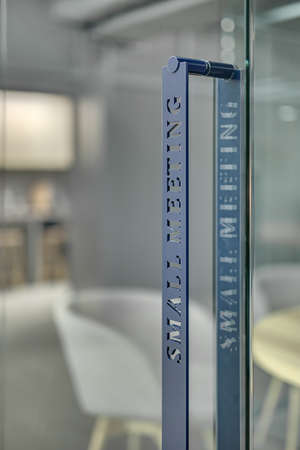 Closeup photo of the door handle on the blurry background. On the handle there is an inscription Small Meeting. Door is glass. Vertical.の写真素材