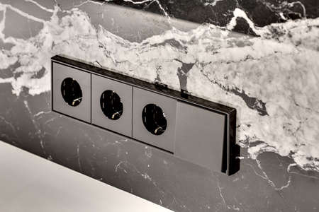 Black power sockets with the switch on the black marble wall with the white patterns. Closeup....