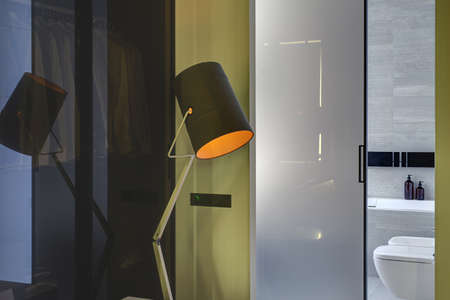 Glowing design lamp on the background of the entrance to the modern bathroom with a glassy door. Bathroom tiled with gray and white tiles. There is a white bath, white toilet and a bide. Horizontal.の写真素材