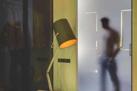 Man's silhouette who is behind the frosted glassy door in the glowing modern interior with yellow walls. In front of the door there is a luminous lamp with an orange lampshade and a glass partition.の写真素材