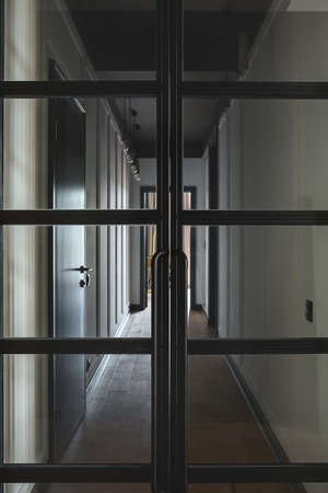 Closed black glass doors on the background of the modern style corridor with white walls and a parquet on the floor. There are another doors, hanging lamps on the ceiling. Closeup. Vertical.の写真素材