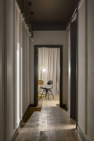 Modern corridor with light walls, doors, hanging lamps and a parquet on the floor. There is an entrance to the room with a wooden table, black chair with gray pillow and a glowing trendy yellow lamp.の写真素材