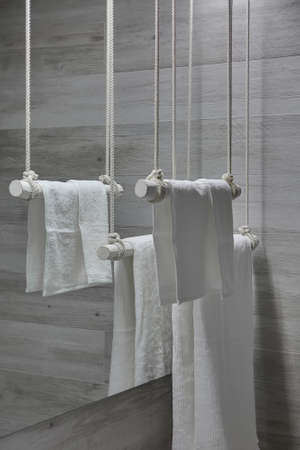 Hanging white wooden towel holders with white towels on the mirror background in the modern bathroom with gray wooden walls. Closeup. Vertical.の写真素材