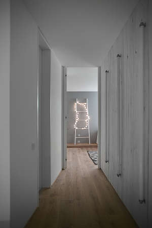 Corridor to the room in the interior in a modern style with white walls and a parquet with a carpet on the floor. There is a white ladder with glowing sphere lamps, doors, tube lamps on a wooden wall.の写真素材