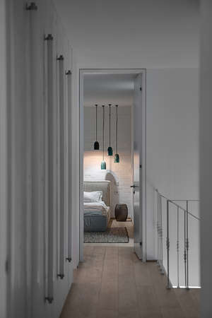 Entrance to the bedroom in the interior in a modern style with white walls and a parquet with a carpet on the floor. There is a bed, lampshade, glowing lamps, tube lamps on the wall, metal railing. の写真素材