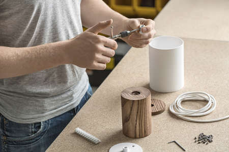 Specialist is using a t-wrench on the metal white detail in the workshop. On the table there are wooden and metal cylindrical billets, cable, connector and bushings. Closeup. Horizontal.の写真素材